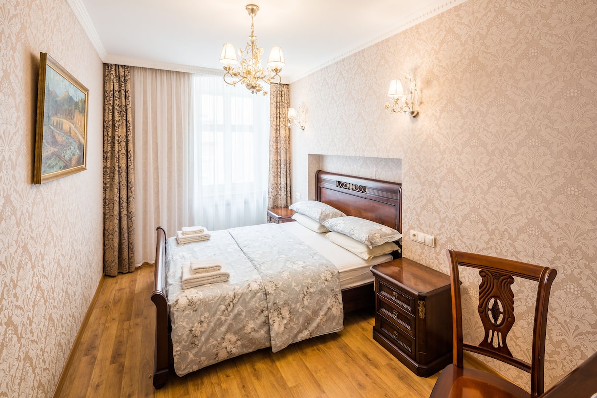 Quarto bem arrumado com uma cama grande, cômoda de madeira, uma cadeira e um lustre.