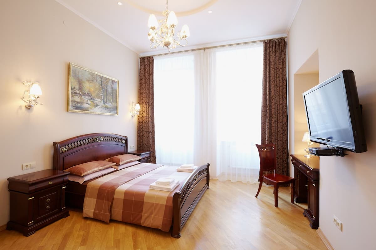 Quarto de hotel com cama de madeira, escrivaninha com televisão, pintura na parede e lustre.