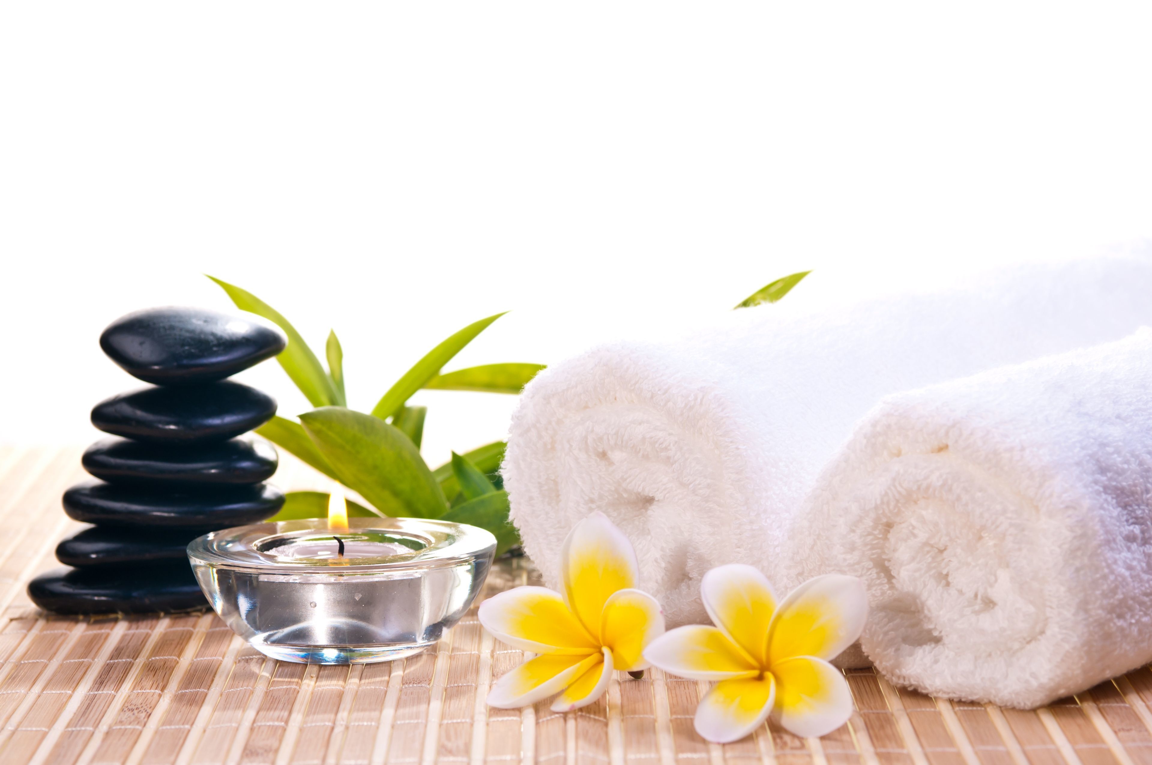 Un espace de bien-être avec une pile de pierres noires, une bougie allumée, des serviettes blanches et des fleurs jaunes et blanches.