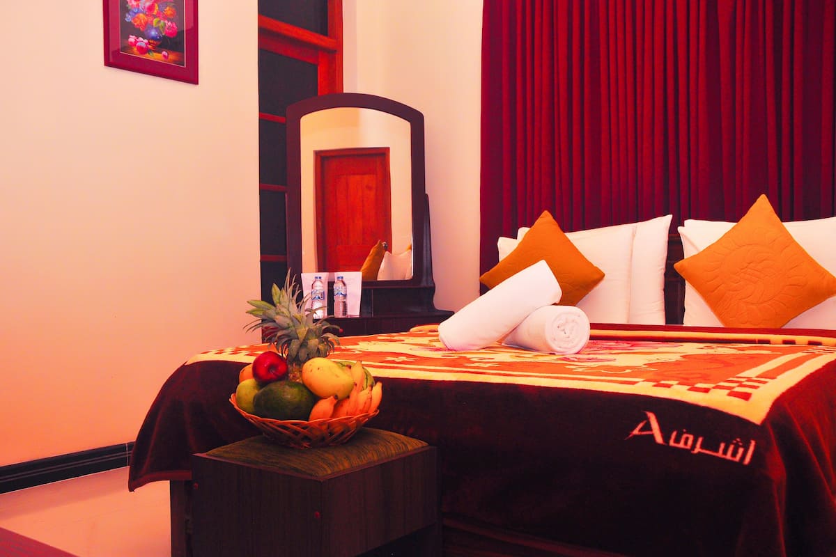 A hotel room with a bed, a fruit basket, a bottle, and a red curtain.