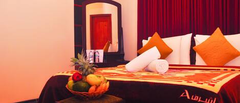 A hotel room with a bed, a fruit basket, a bottle, and a red curtain.
