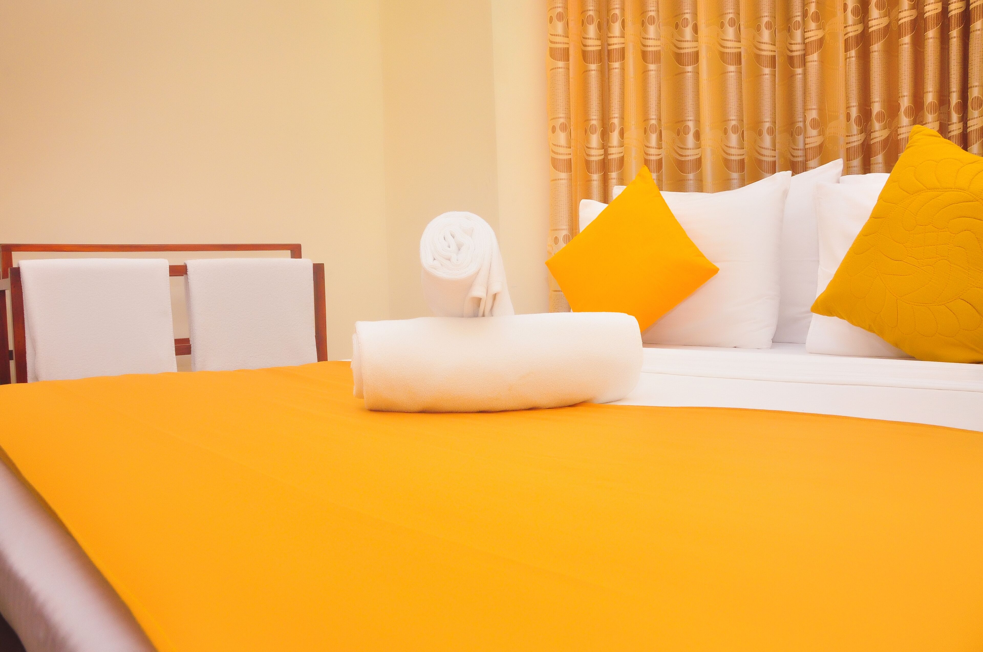 A neatly made bed with a white and yellow color scheme, a rolled white towel, and a pillow with a yellow pillowcase.