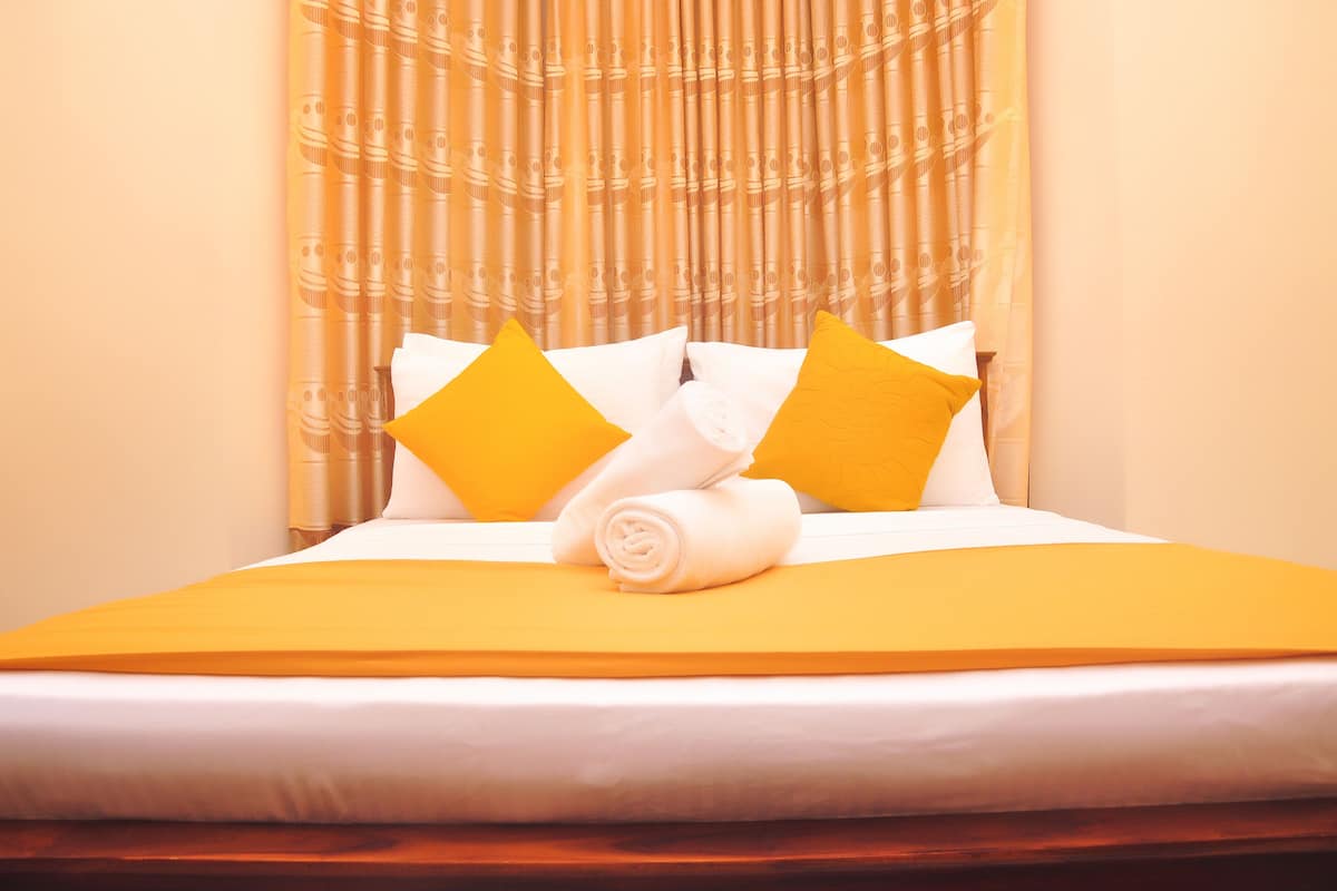 A neatly made bed with white and yellow bedding, a rolled towel, and two pillows.