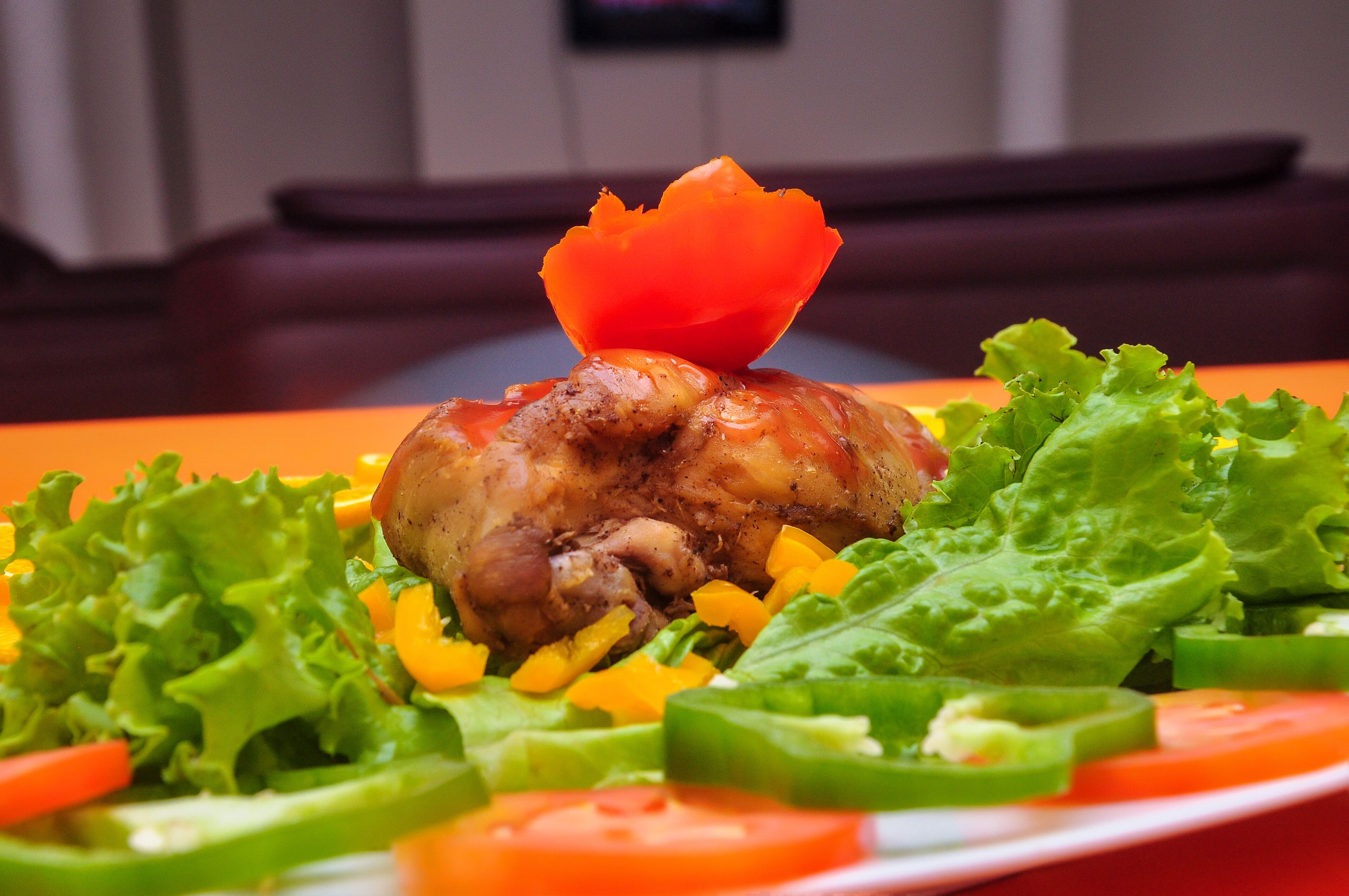 Een bord eten met vlees, groenten en een decoratieve tomaat.