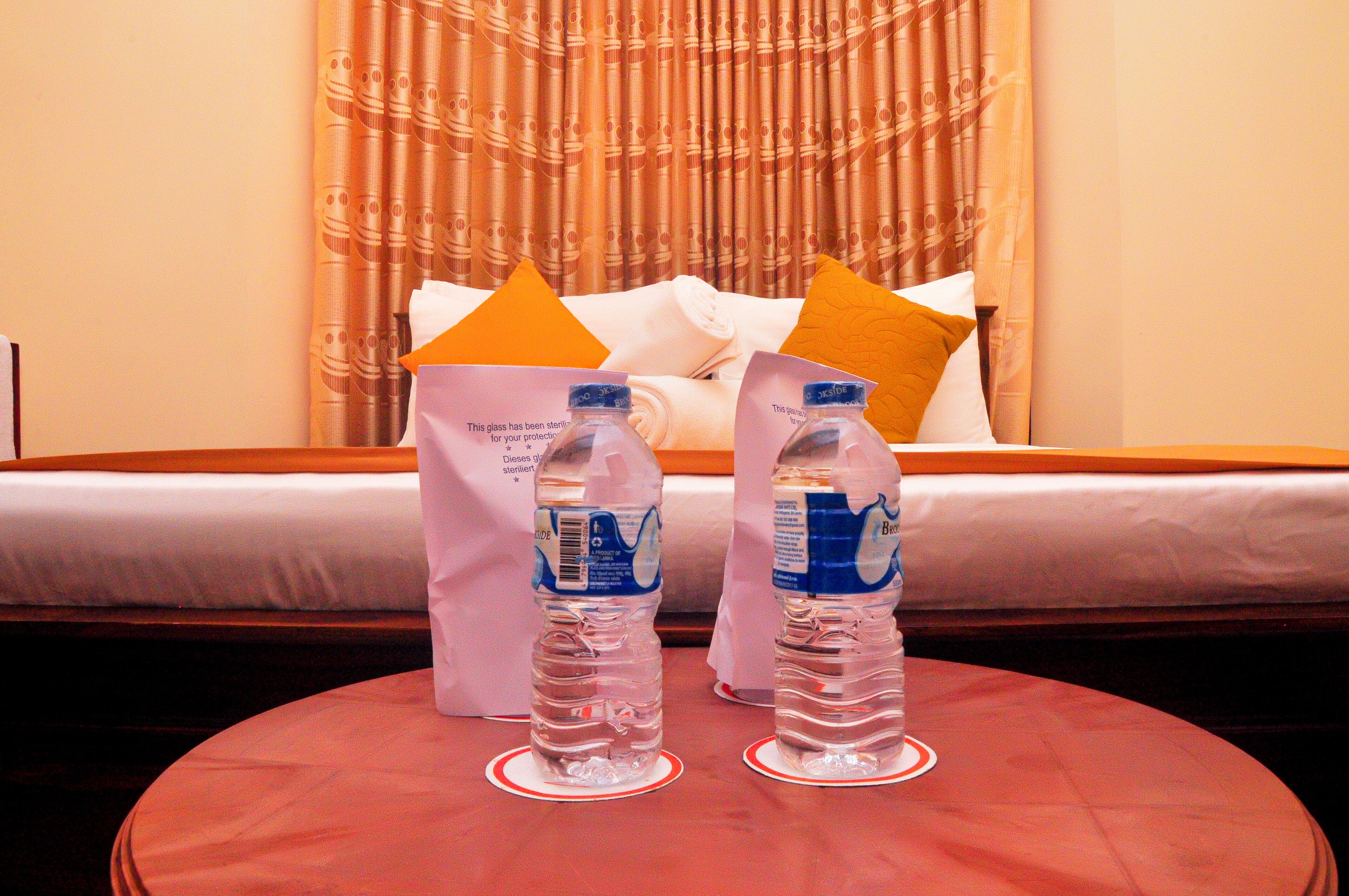 A hotel room with a bed, pillows, and two water bottles on a table.
