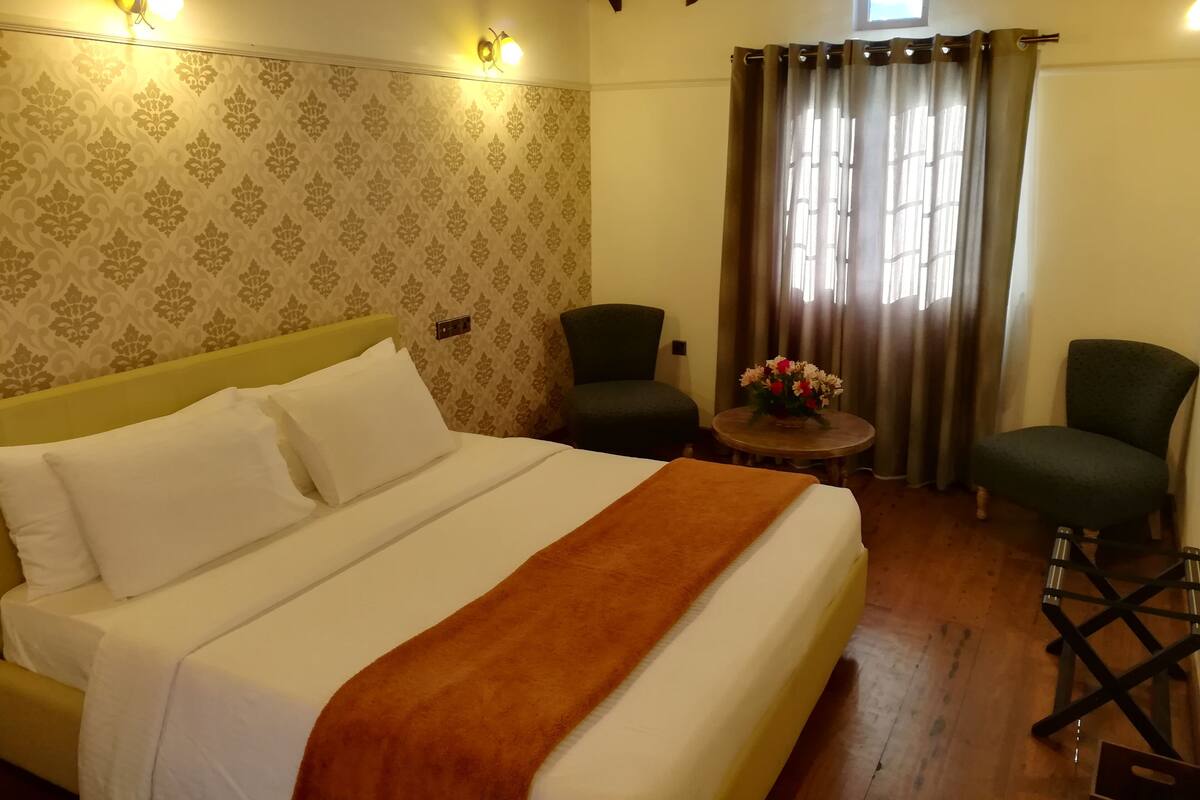 A hotel room with a bed, two chairs, a small table with flowers, and a window with curtains.