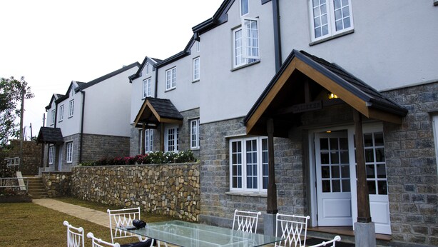 A two-story building with a stone facade, a glass door entrance, and a small outdoor seating area with a table and chairs. - The Planter's Legacy By Fairway (Nuwara Eliya)