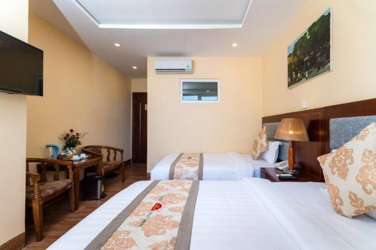 Een hotelkamer met twee bedden, een bureau met stoel, een televisie, een airconditioner en een schilderij aan de muur.