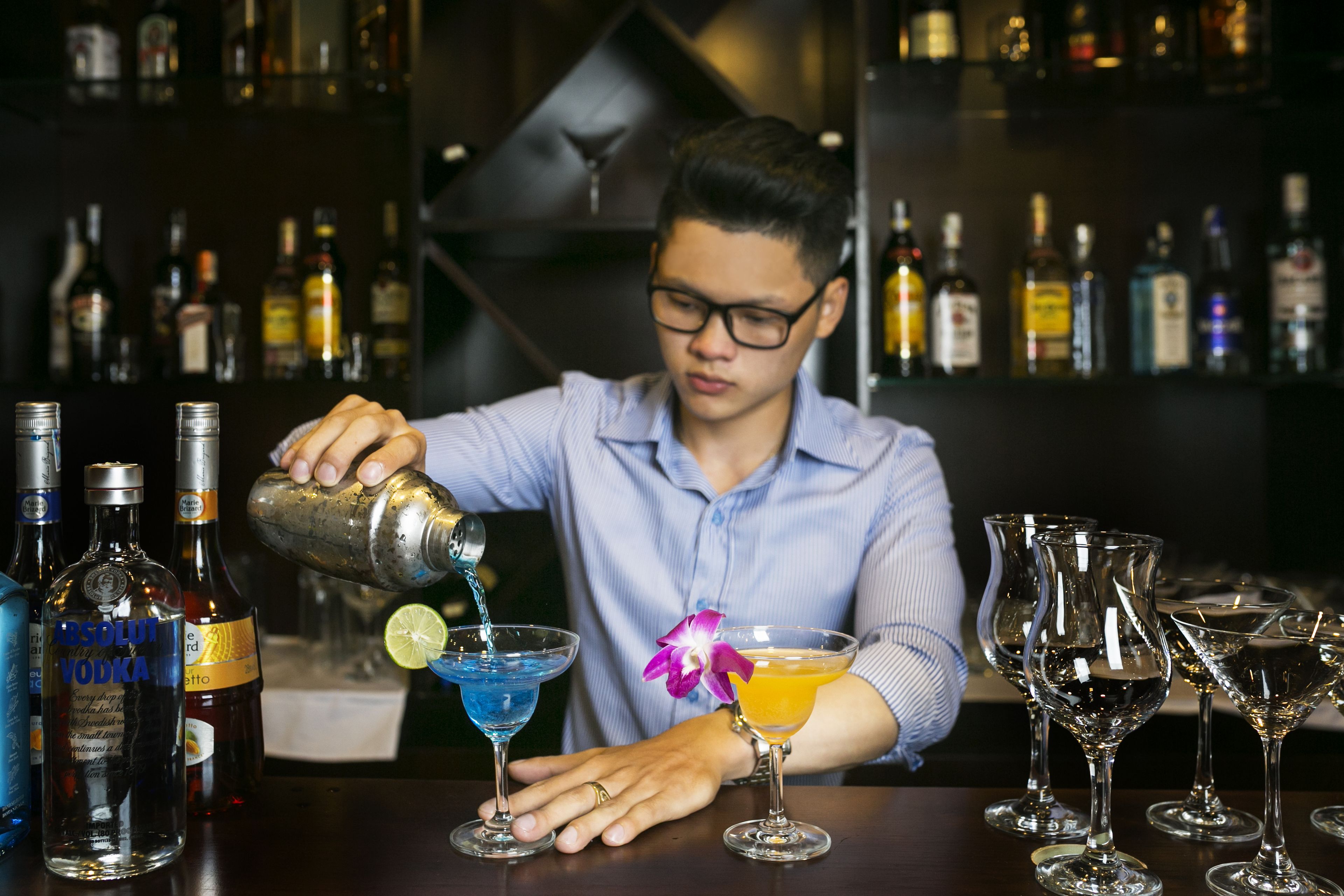 A bartender pouring a drink into a martini glass.