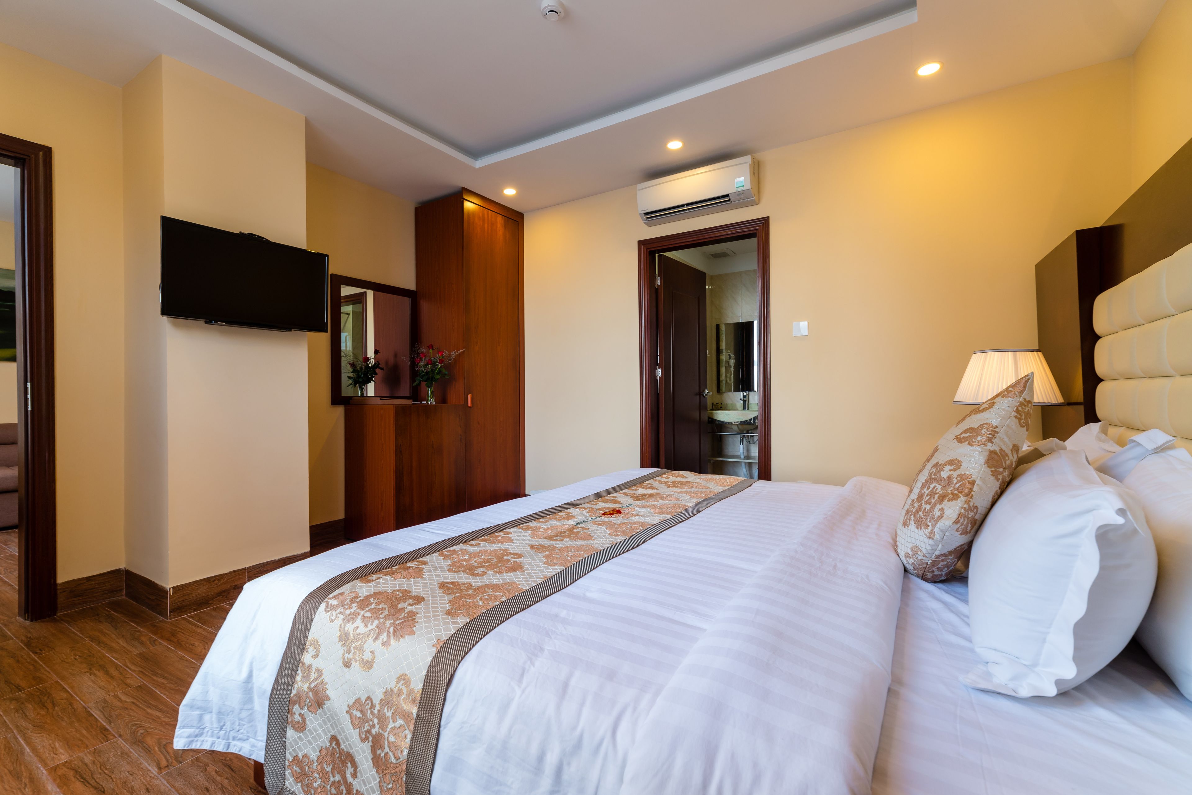 Een hotelkamer met een groot bed, een flatscreen televisie aan de wand, een houten garderobe en een airconditioner.