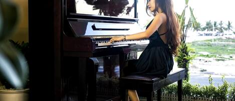 A woman playing a grand piano in a room with a view of a tropical landscape.