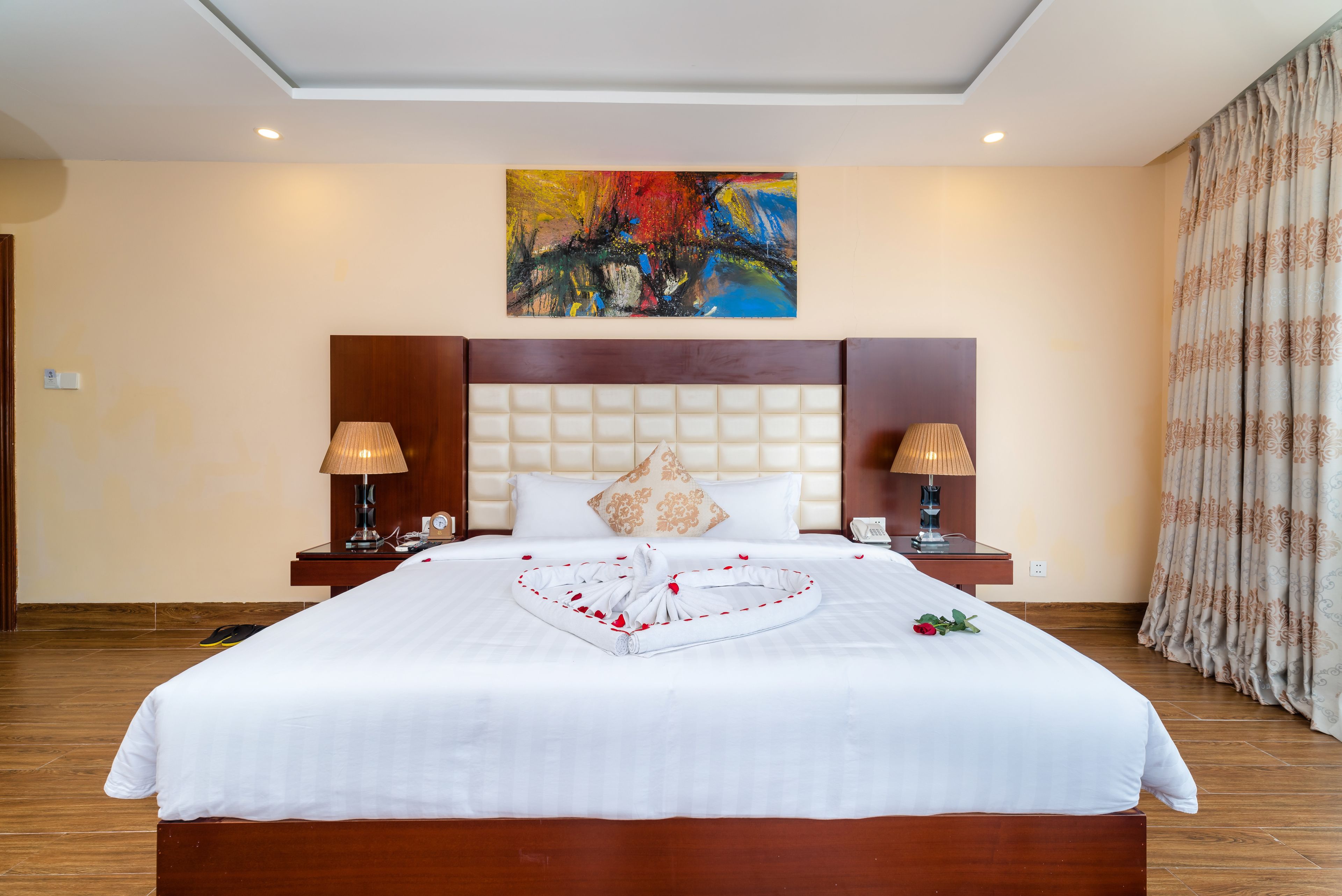 Habitación de hotel con una cama grande, dos lámparas de noche, un cuadro en la pared y una cortina en la ventana.