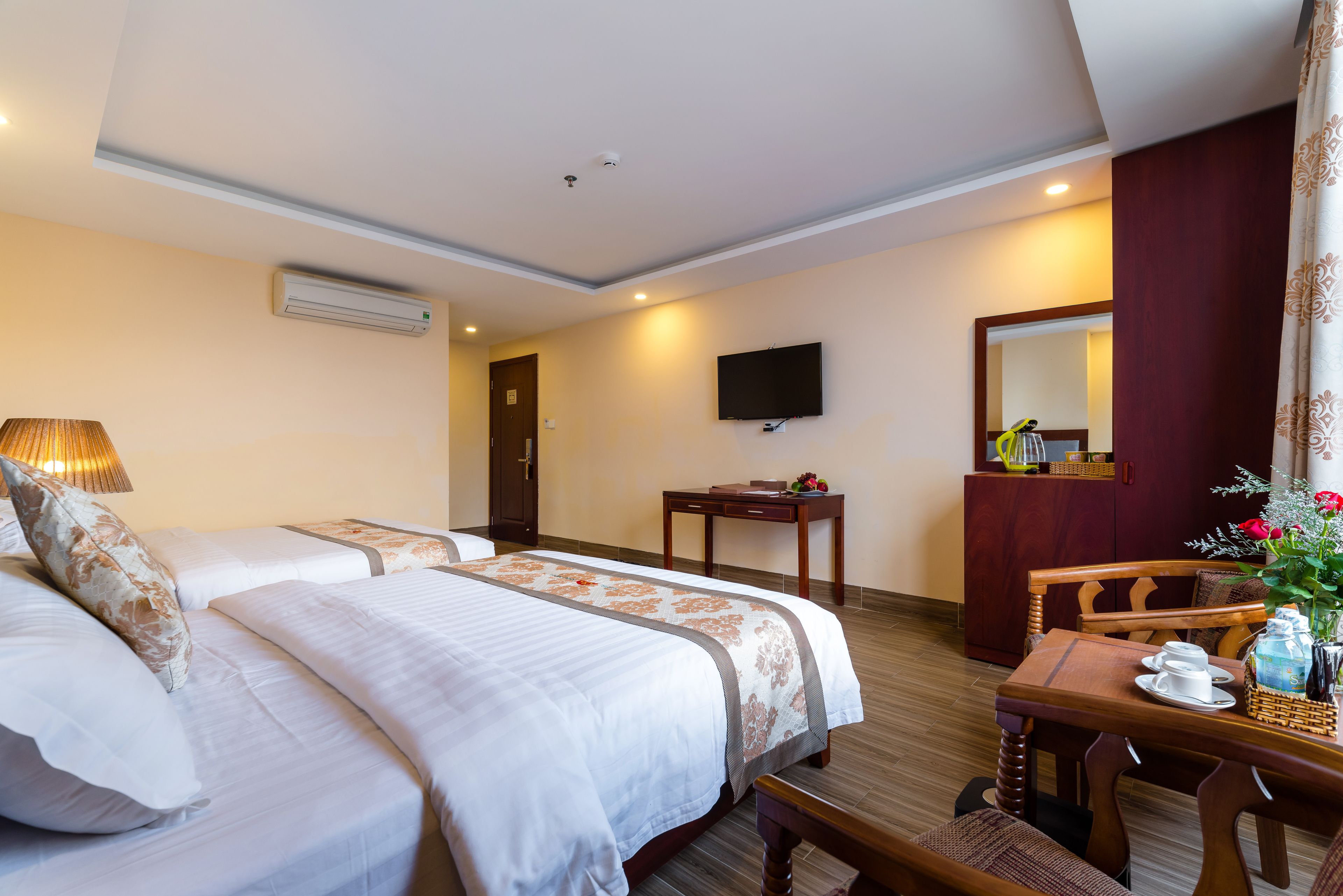 A hotel room with two beds, a desk, a chair, a television, and a mirror.