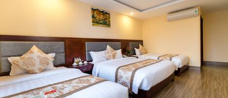 A hotel room with three beds, a headboard, a painting on the wall, and an air conditioning unit.