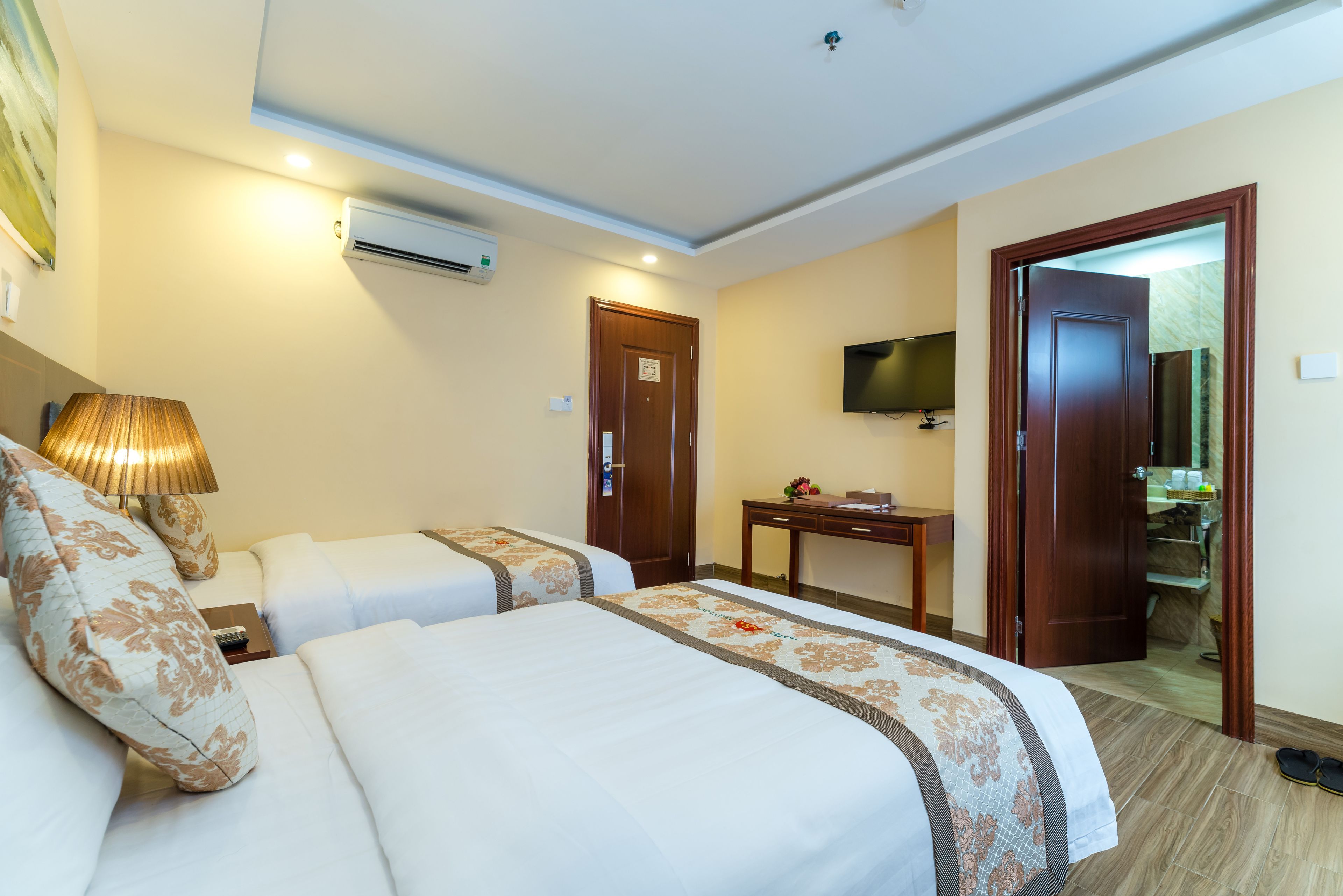 A hotel room with two beds, a desk, a TV, and an air conditioning unit.