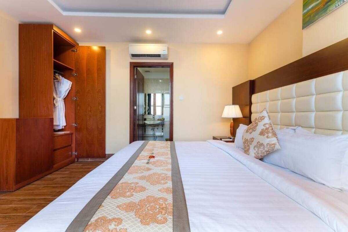 Een hotelkamer met een groot bed, een houten garderobe, een nachtkastje met lamp en een airconditioning aan de muur.