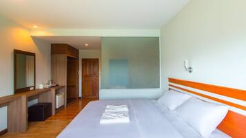 A hotel room with a large bed, a wooden headboard, a mirror, a desk with a chair, and a wardrobe.