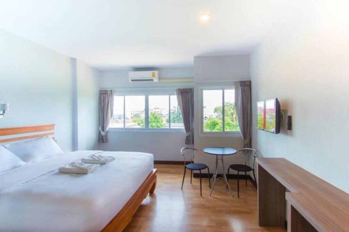 A hotel room with a bed, a desk, two chairs, a TV, and a window with curtains.