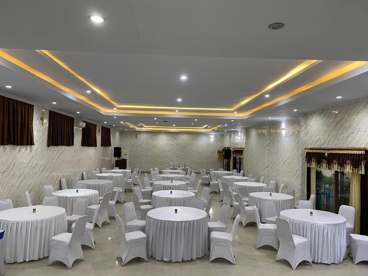 A conference room with round tables and white chairs, marble walls, and recessed lighting.