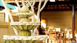 A multi-tiered stone fountain with water cascading down, set in a well-lit indoor area with wooden beams and a tiled floor.