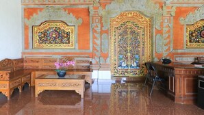 A room with ornate wall decorations, a wooden bench, a table with a vase, and a desk with a chair.
