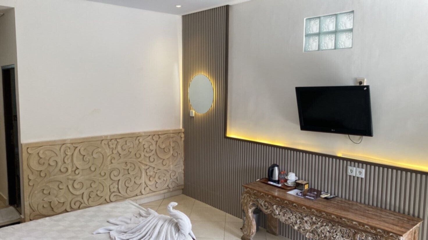 Ein Hotelzimmer mit einem Bett, einem Holzschranken mit Flachbildfernseher, einem Wandspiegel und einem dekorativen Kopfteil.