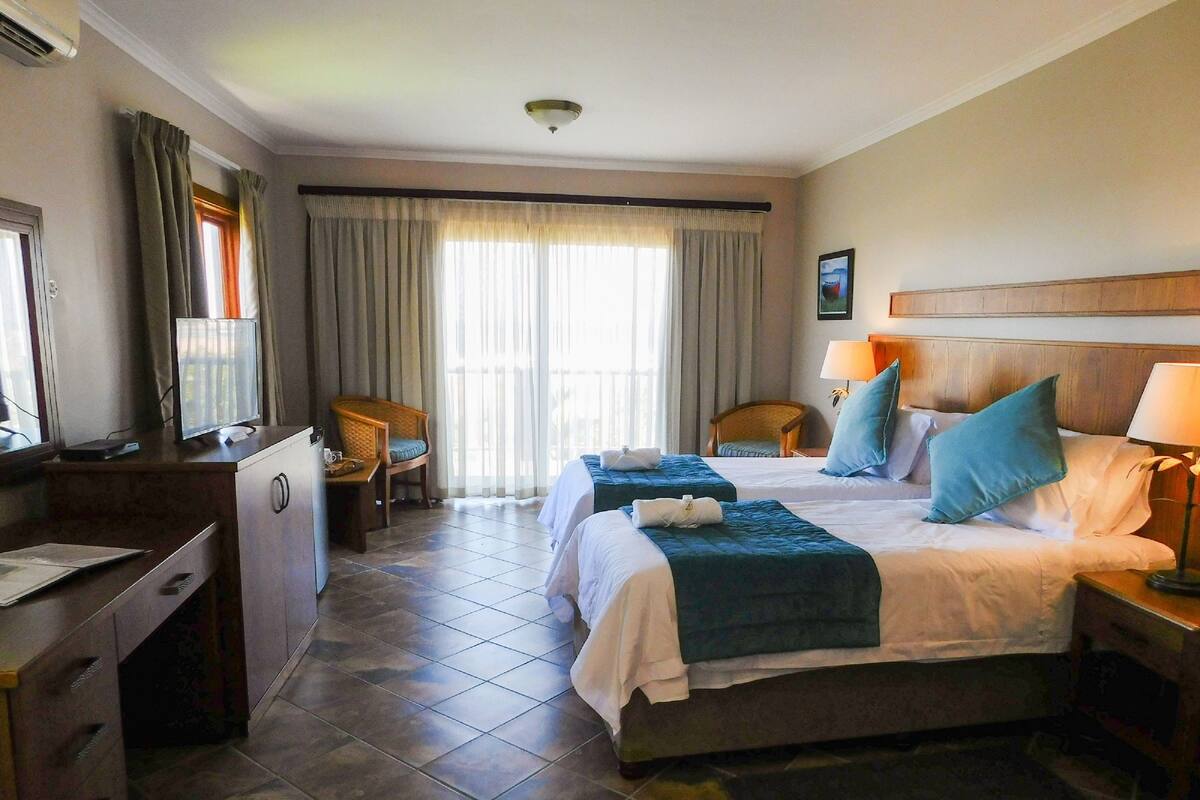 Habitación de hotel con dos camas, un escritorio, una silla, un televisor y una ventana con cortinas.