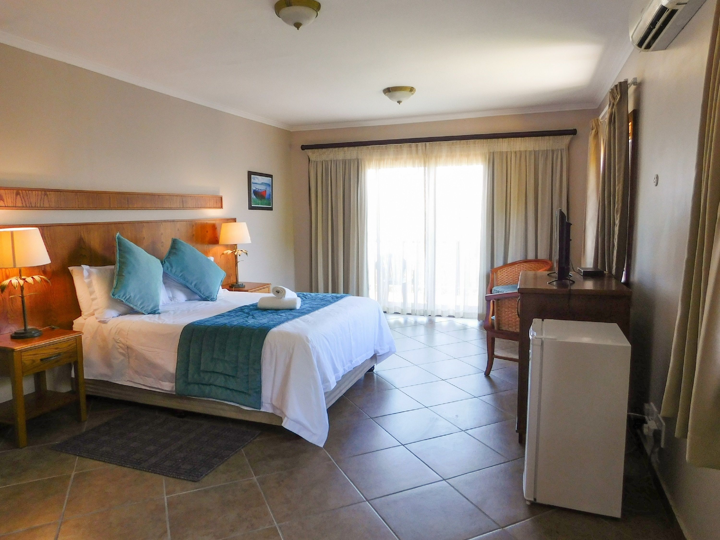 Habitación de hotel con cama, dos lámparas de noche, escritorio con silla, televisión y ventana con cortinas.