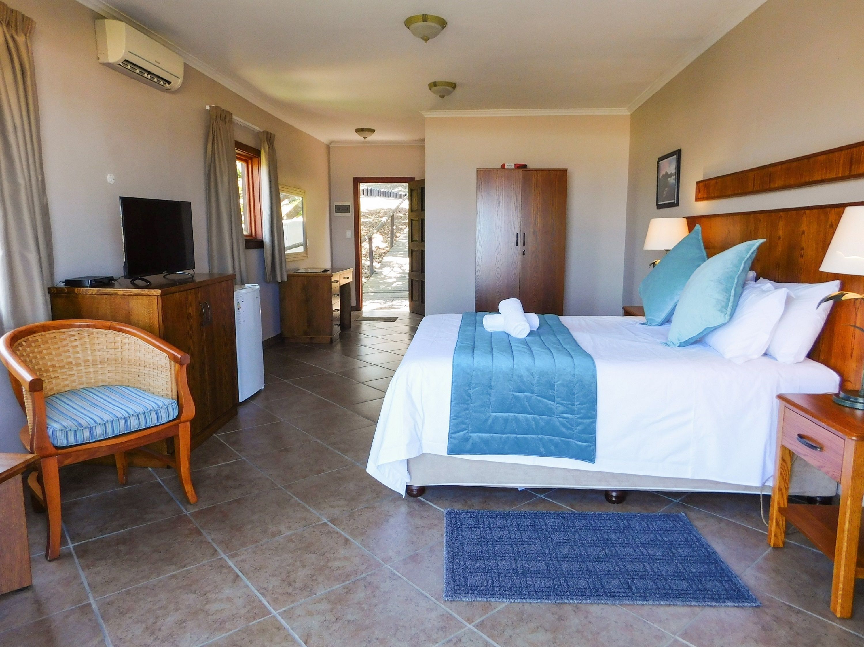 A hotel room with a bed, a desk, a chair, a television, and an air conditioning unit.