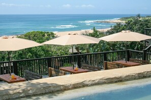 Eine Terrasse mit Sitzgelegenheiten im Freien, einem Pool und Blick auf den Ozean und den Strand.