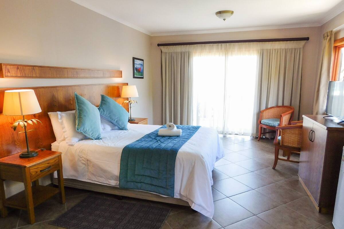 Habitación de hotel con una cama grande, dos mesitas de noche, un escritorio, una silla y una ventana con cortinas.