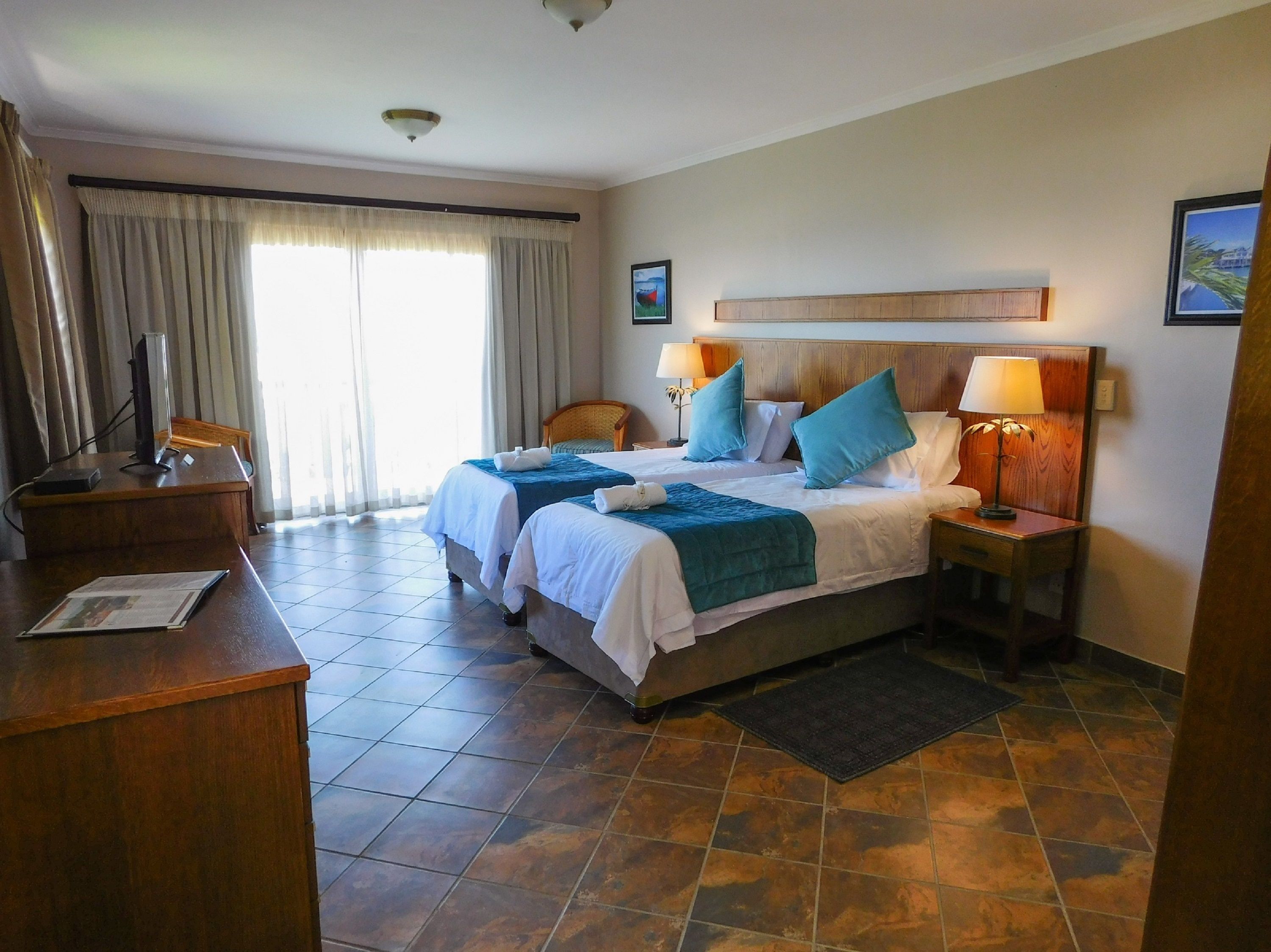 Habitación de hotel con dos camas, un escritorio, una silla, una lámpara y una ventana con cortinas.
