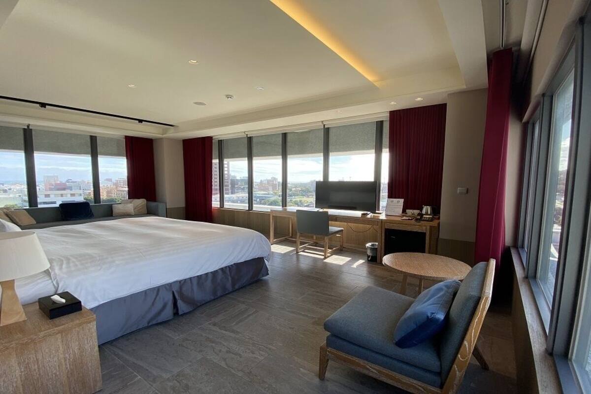 Et moderne hotelværelse med en stor seng, et skrivebord, en stol og udsigt over byen.
