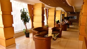 A hotel lobby with leather sofas, a glass coffee table, potted plants, and a TV screen. - Kıvrak Hotel (Antalya)