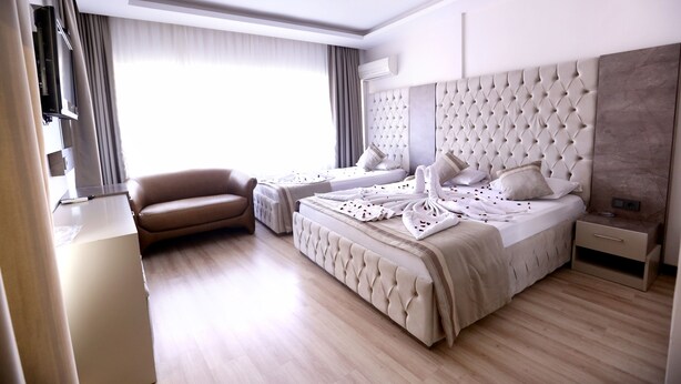 A modern hotel room with a large bed, a sofa, a TV, and a desk. - Kıvrak Hotel (Antalya)