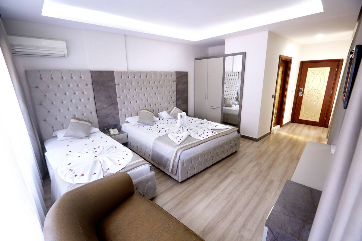 A hotel room with two beds, a sofa, a wardrobe, and a mirror.