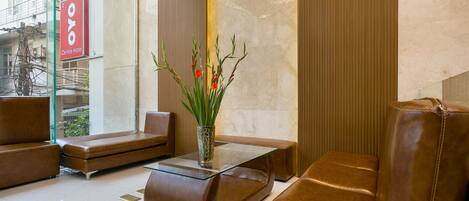 Un lobby moderno con sofás de cuero, una mesa de centro de vidrio y un jarrón con flores rojas.