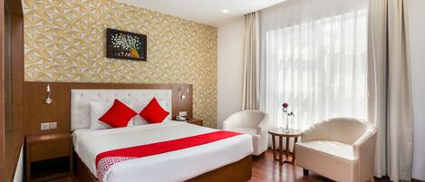 Una habitación de hotel con una cama grande, una silla, una mesita y una ventana con cortinas.