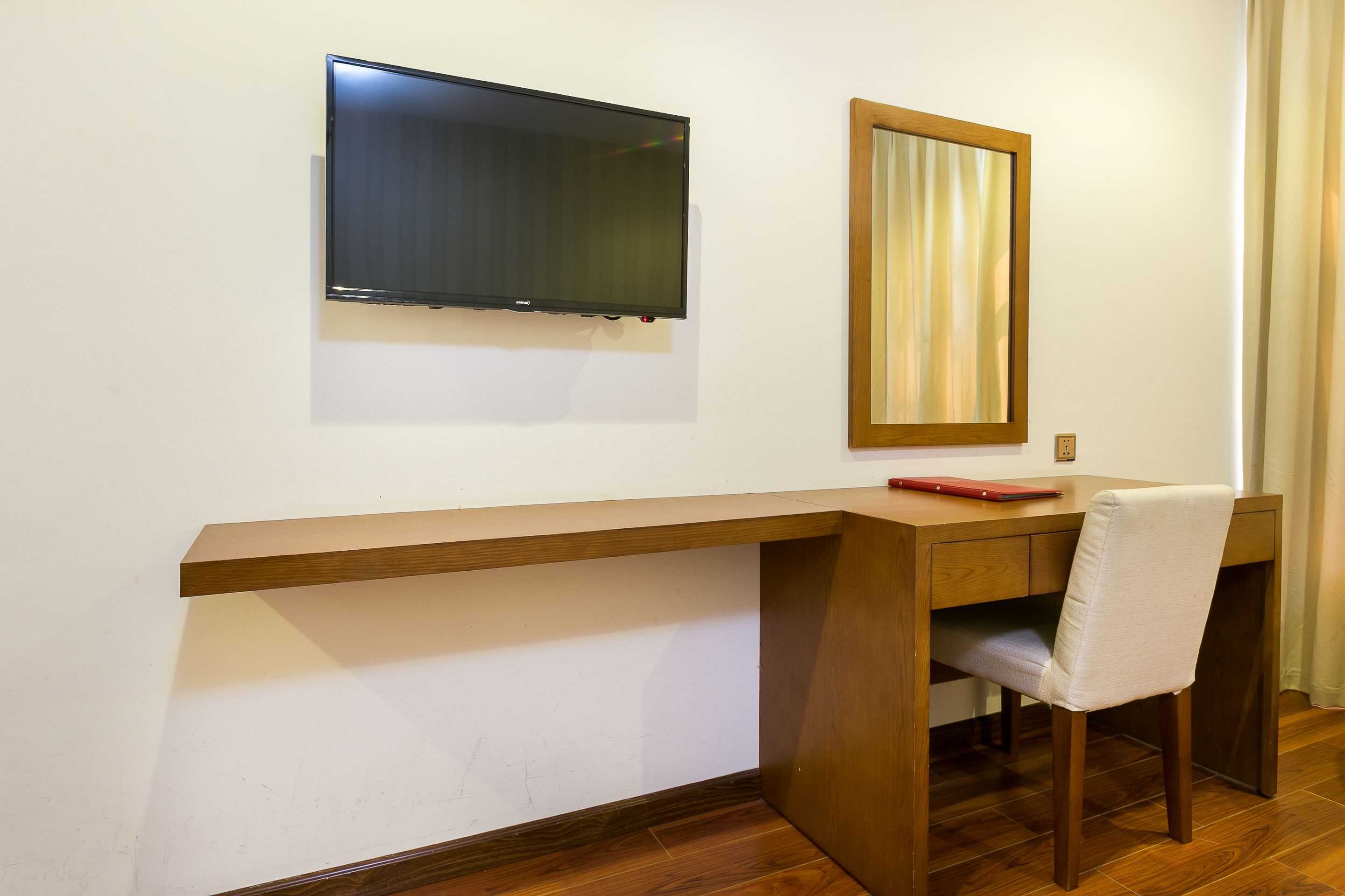 Un escritorio de madera con una silla, un televisor montado en la pared y un espejo.