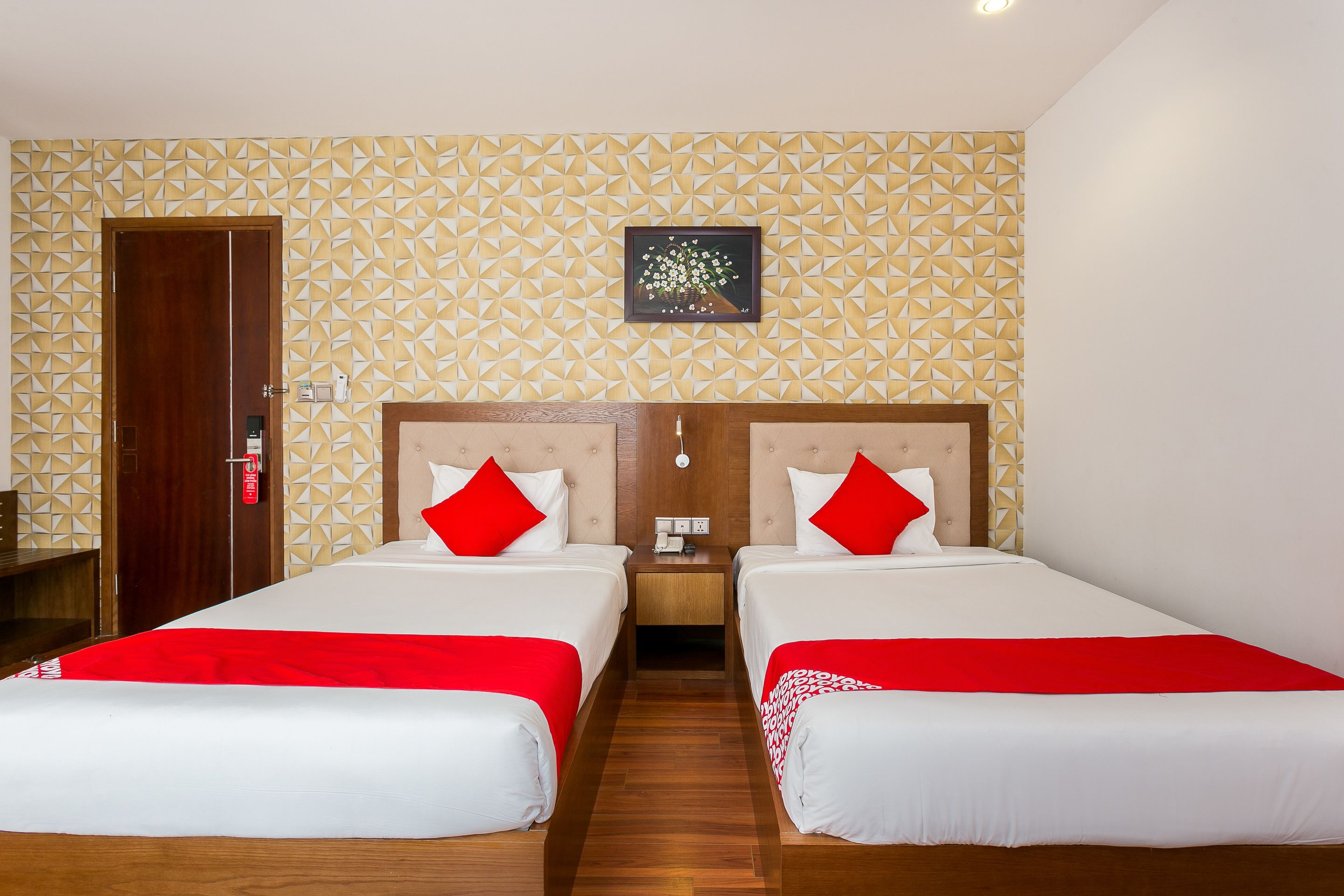 Ein Hotelzimmer mit zwei Betten, jeweils mit roter und weißer Bettwäsche, einem Holz-Kopfteil und einer Wand mit geometrischem Muster.