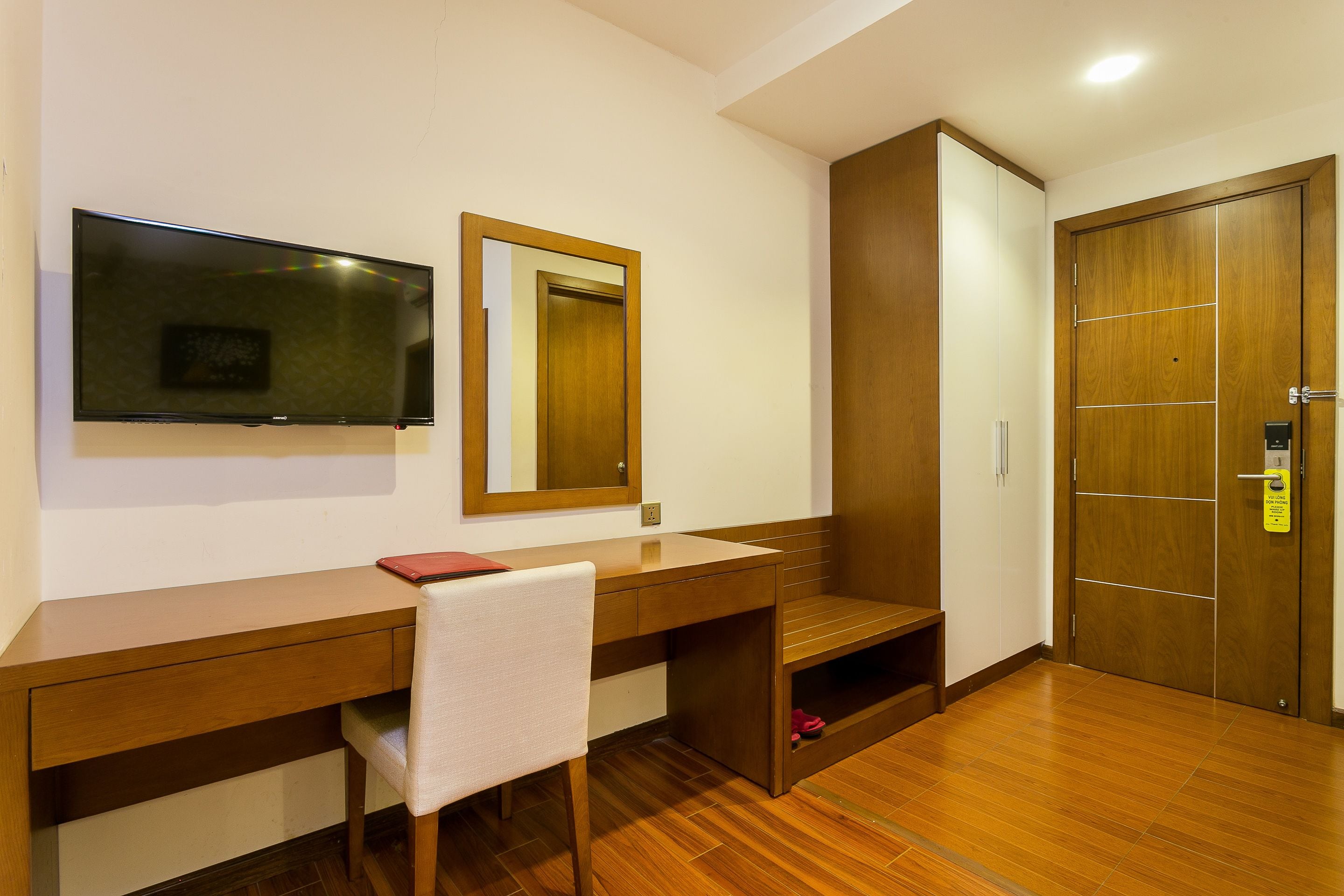 Une chambre d’hôtel avec un bureau en bois, une chaise, un miroir, une armoire et une porte.