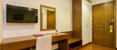 A hotel room with a wooden desk, a chair, a mirror, a wardrobe, and a door.