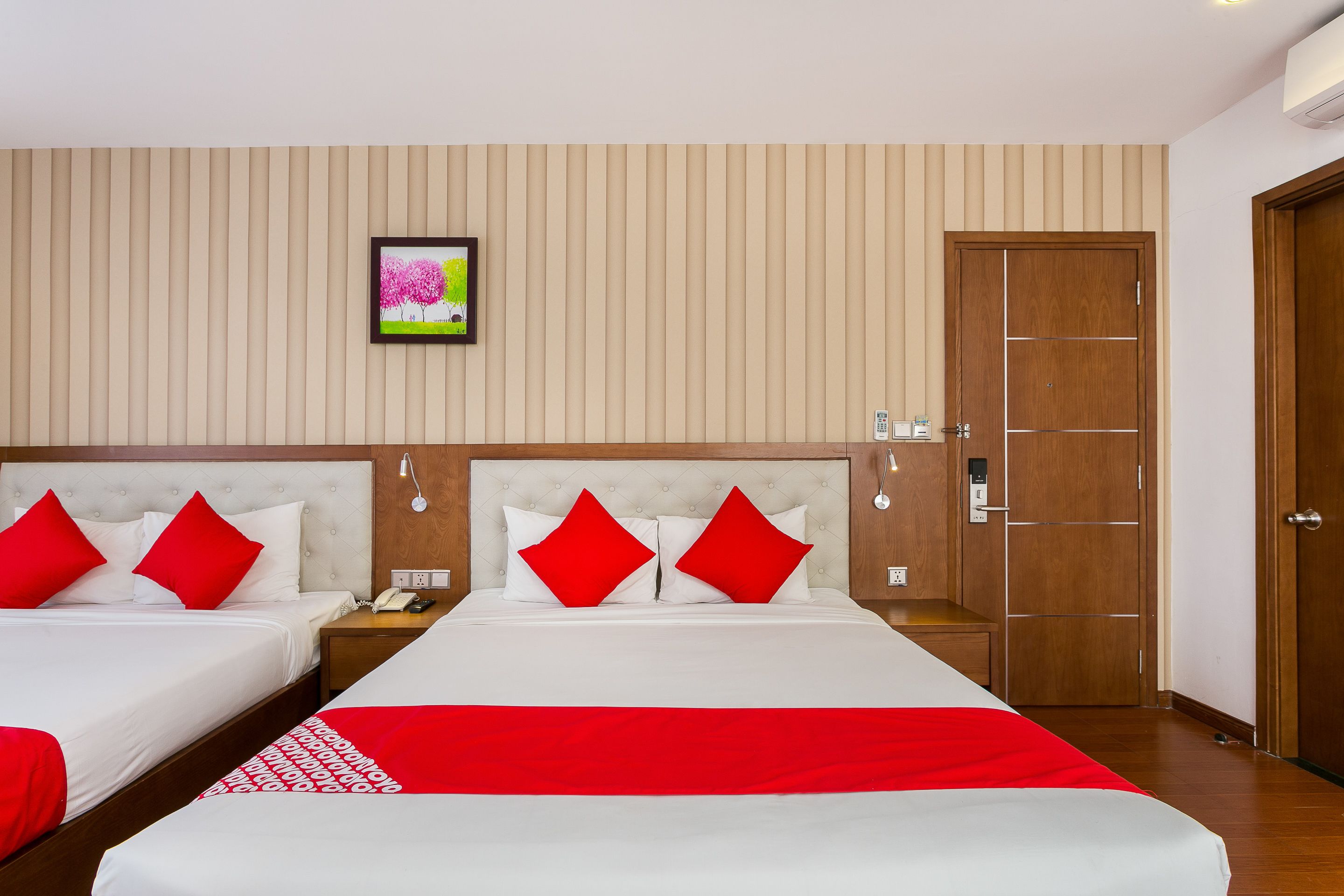 A hotel room with two beds, each with red and white bedding, a wooden headboard, a framed picture on the wall, and a wooden door.