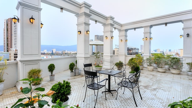 Terraço no telhado com mesa e cadeiras, plantas em vasos e vista para a cidade.