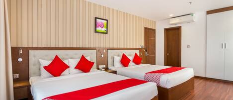 A hotel room with two beds, each with red and white bedding, a wooden headboard, a wall-mounted air conditioner, and a framed picture above the beds.
