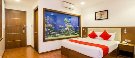 Una habitación de hotel con un acuario grande, una cama con almohadas rojas y suelo de madera.