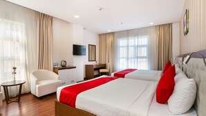 Quarto de hotel com duas camas, uma escrivaninha, uma cadeira e uma televisão.