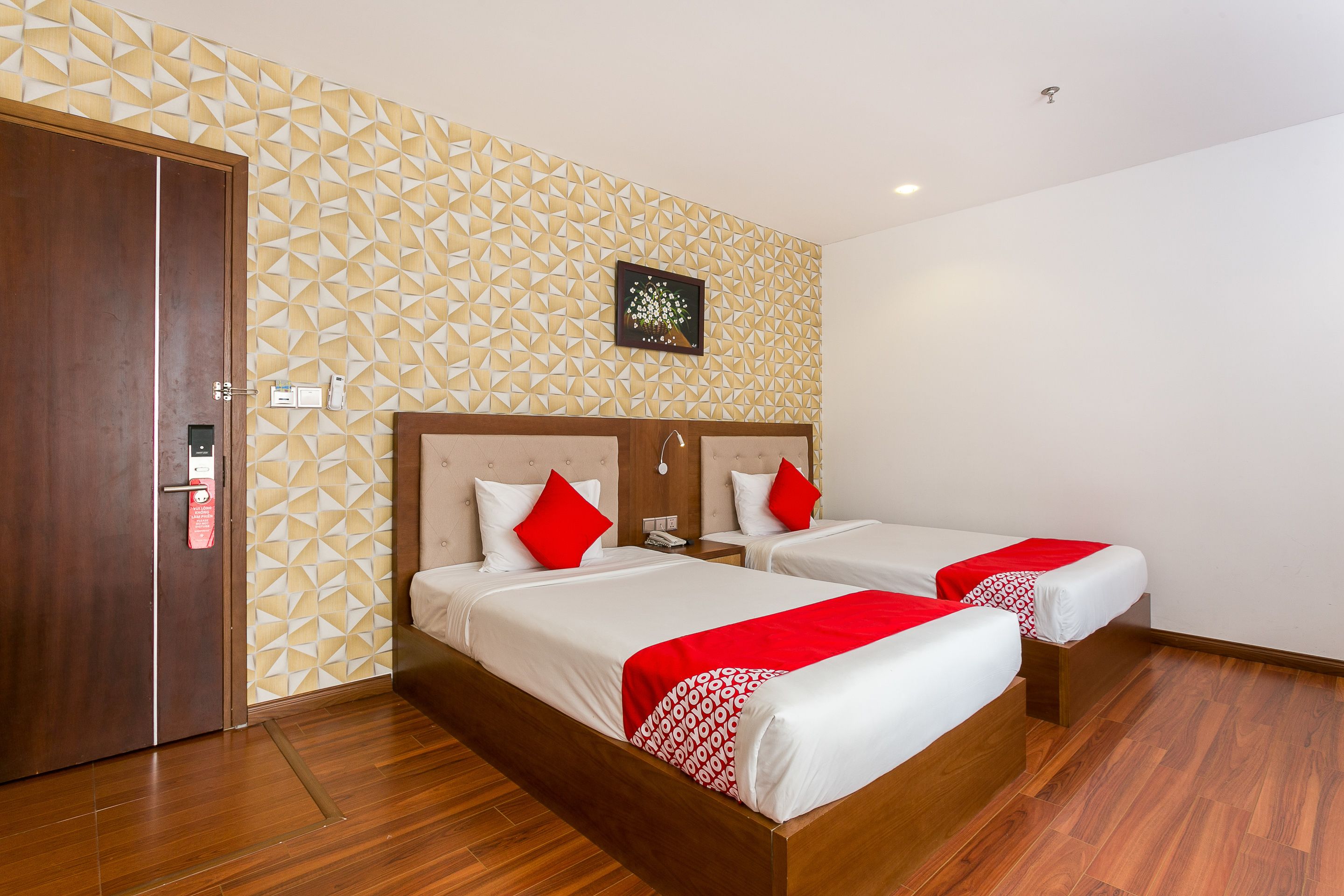 Ein Hotelzimmer mit zwei Betten, Holzboden, einer Wand mit geometrischem Muster und einem Bild über den Betten.
