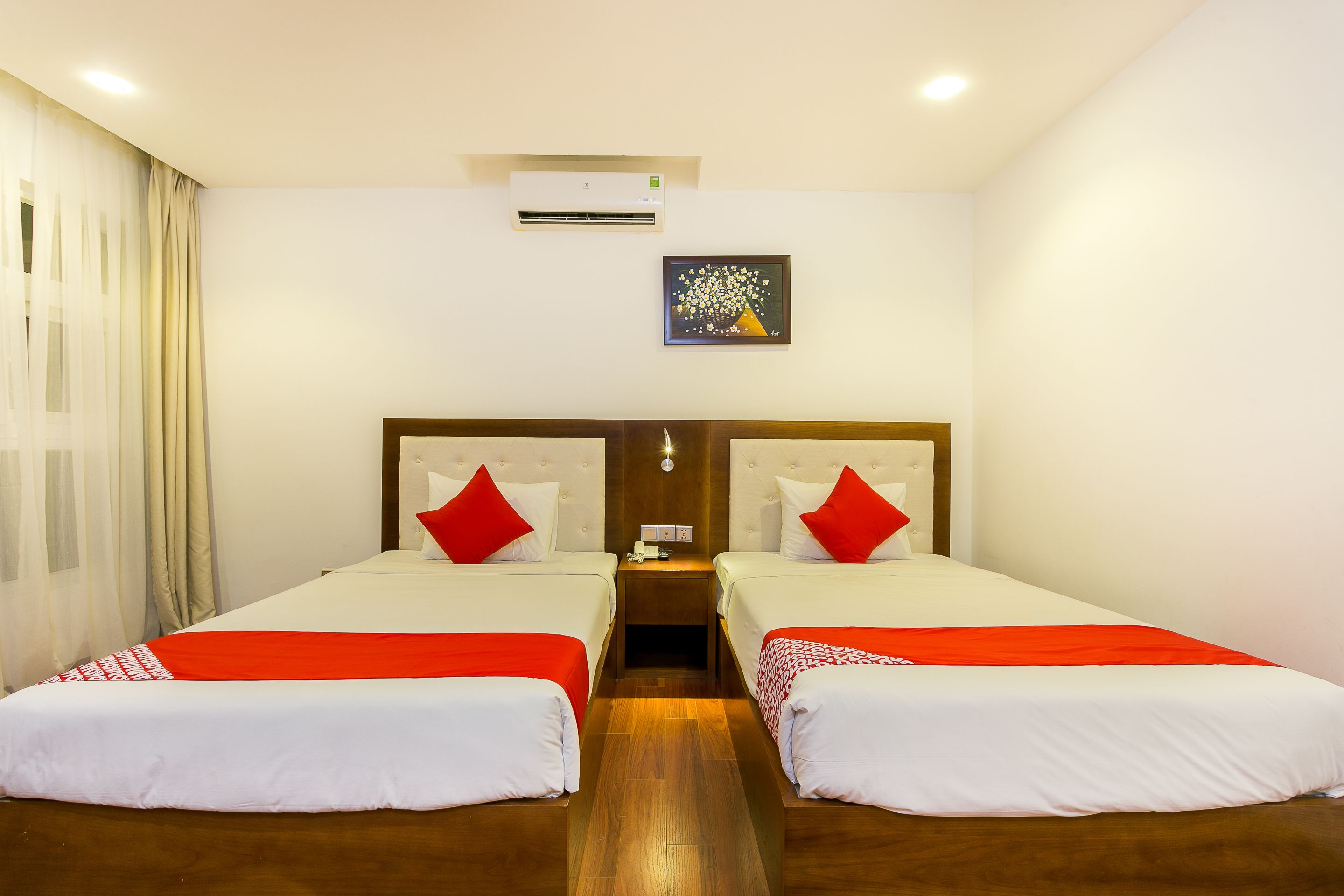 A hotel room with two beds, a nightstand, an air conditioning unit, and a painting on the wall.