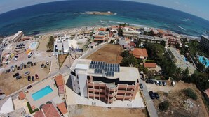 An aerial view of a coastal area with buildings, a swimming pool, and solar panels. - Artemis Bay by Estia (Hersonissos)